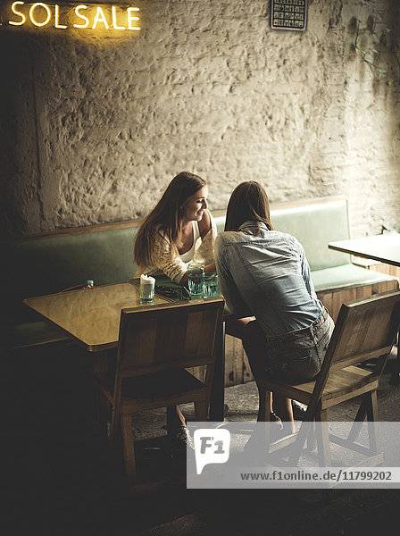 Zwei junge Frauen sitzen an einem Cafétisch und schauen nach unten.
