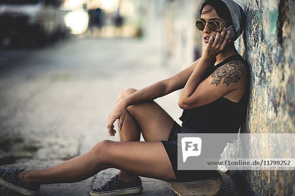 Young woman sitting on a skateboard talking on a cellphone.