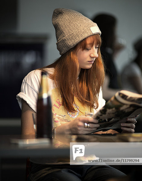 A young woman sitting at a table reading a newspaper.