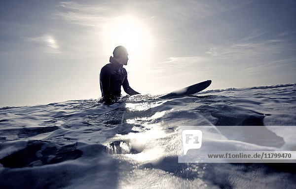 Surfer im Neoprenanzug auf einem Surfbrett im Meer sitzend.