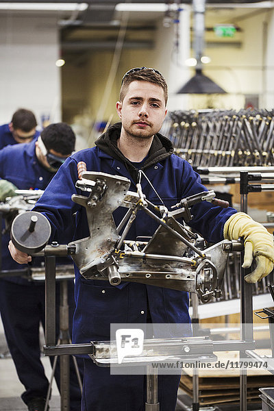 Male skilled factory worker in overalls wearing one protective glove working on a bicycle frame in a factory.