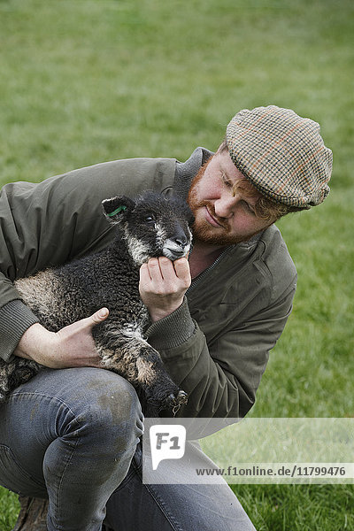 Ein Landwirt  der ein junges Lamm im Arm hält und nach dem Tier sieht.