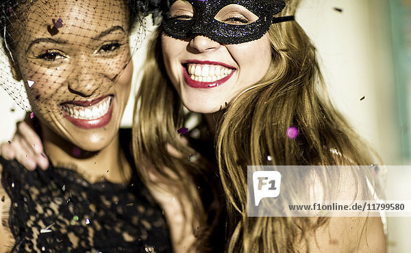 Zwei junge Frauen lachen und winken mit den Armen und tanzen auf einer Glitzerparty.