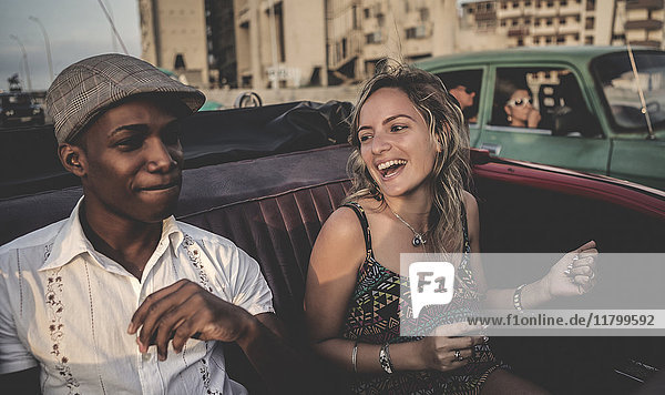 Two people riding through an urban environment in an open convertible classic car.