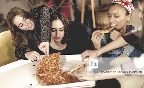 Vier junge Frauen sitzen an einem Tisch und essen Pizza.