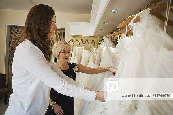 Two women  a young bride to be and a mature sales assistant looking through rails of wedding dresses.
