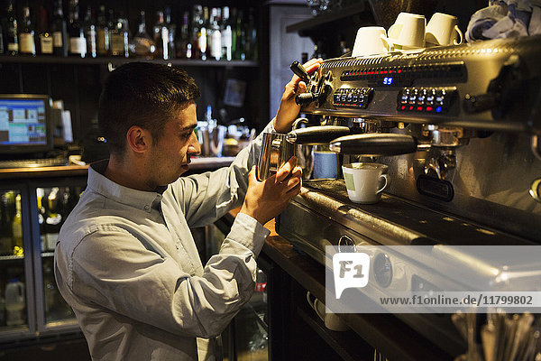Side view of man standing at an espresso machine  frothing milk.