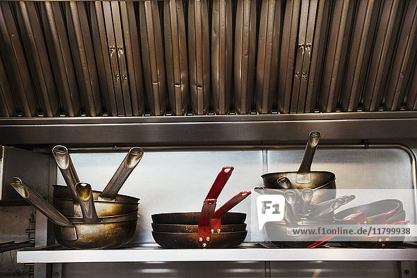 Nahaufnahme eines Stapels von Töpfen und Pfannen auf einem Regal in einer Restaurantküche.