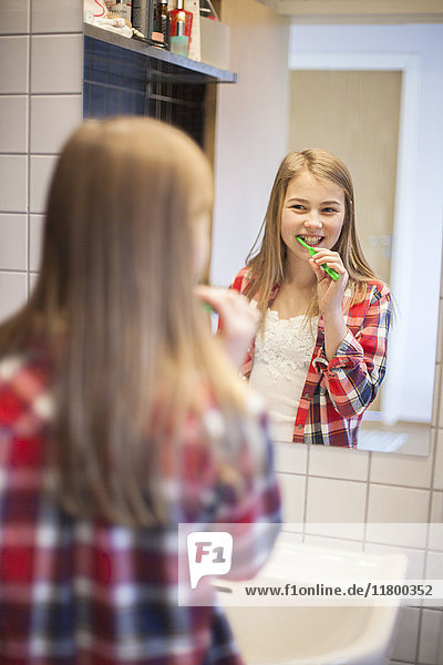 Mädchen putzt sich die Zähne und schaut in den Spiegel