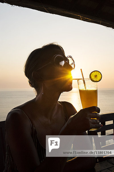 Frau bei Sonnenuntergang mit Cocktail