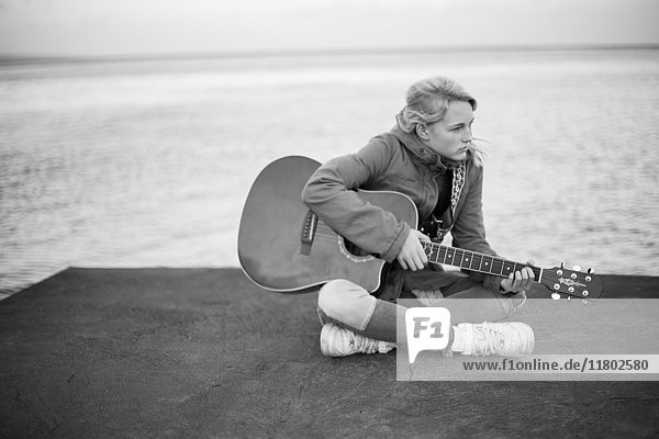 Junge Frau mit Gitarre sitzend  Meer im Hintergrund