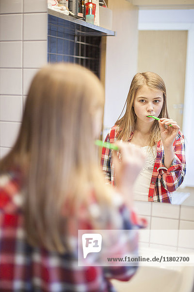 Mädchen putzt sich die Zähne und schaut in den Spiegel