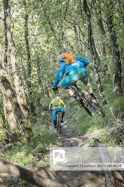 Biker jumping in mid-air while riding bike and following other biker on dirt path