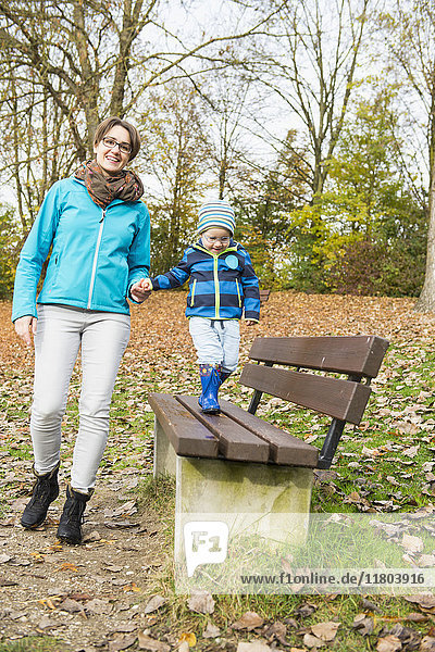 Mother holding hand of her son walking on park bench in autumn