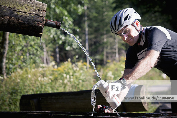 Radfahrer füllt Wasserflasche im Wald