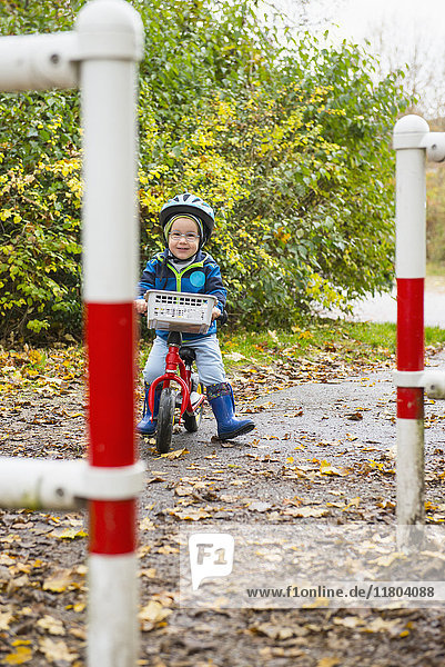 Kleiner Junge fährt mit einem Laufrad durch eine Schranke