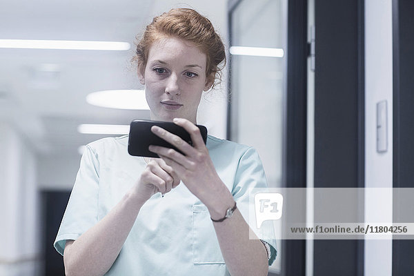 Junge Krankenschwester benutzt Mobiltelefon im Krankenhaus