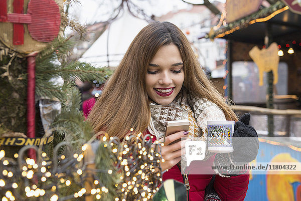 Junge Frau hält eine Tasse und benutzt ein Mobiltelefon