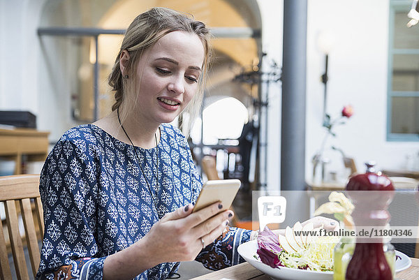 Junge Frau  die ein Mobiltelefon benutzt  während sie im Restaurant sitzt