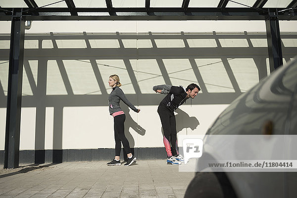 Man and woman in sportswear doing stretching on city footpath