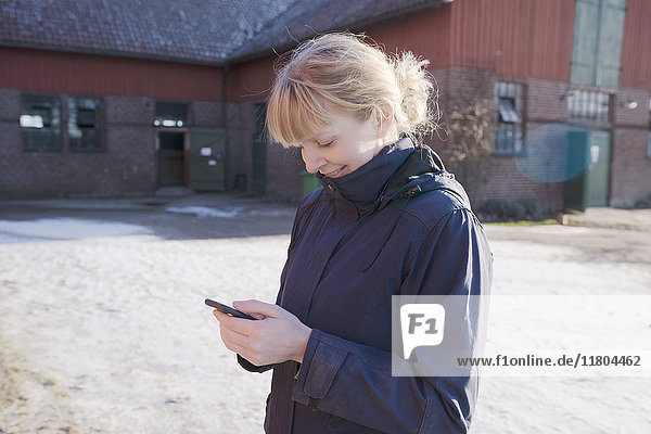 Frau benutzt Mobiltelefon auf einem Bauernhof