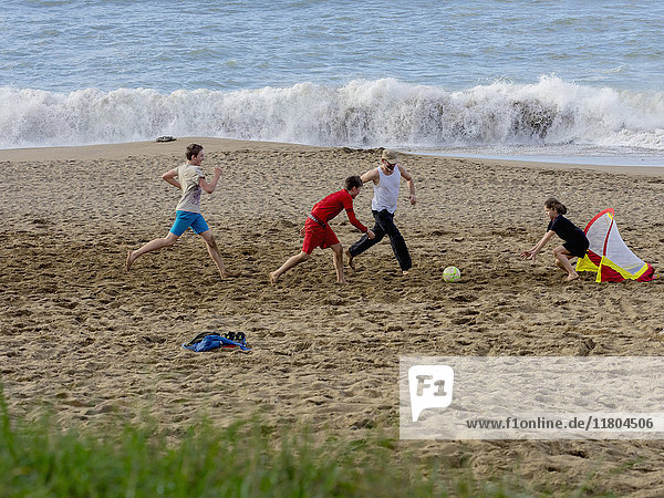 Mädchen und Jungen spielen Fußball mit Vater am Strand