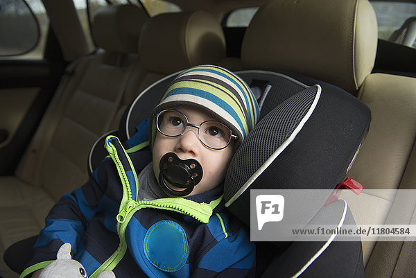 Kleiner Junge mit Schnuller im Mund im Autositz sitzend