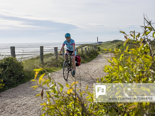 Frau fährt Fahrrad auf einem Weg am Meer