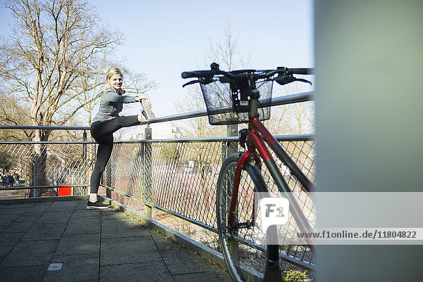 Frau in Sportkleidung beim Stretching auf einer Brücke mit Fahrrad im Vordergrund