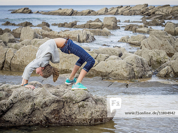Girl in backflip position on rocks at beach
