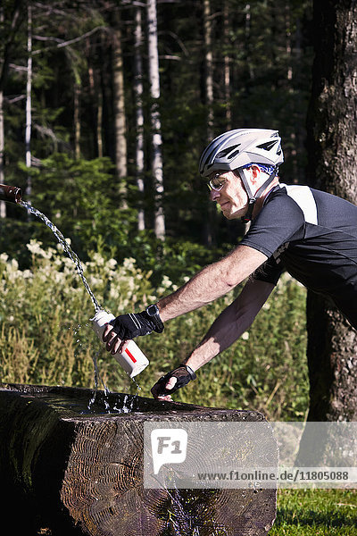 Biker filling water bottle in forest