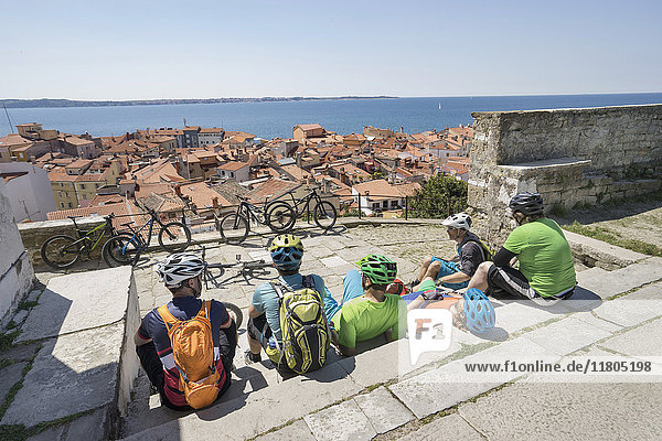Radfahrer  die auf einer Treppe sitzen und eine verstopfte Stadt am Meer betrachten