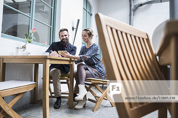 Lächelndes junges Paar benutzt Mobiltelefon in einem Café