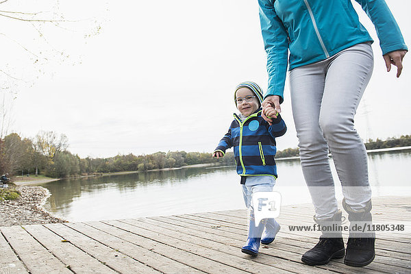 Mother and son walking hand in hand on a landing stage over lake in autumn