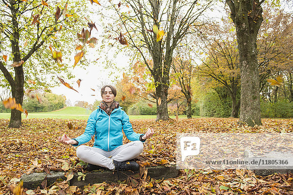 Frau meditiert auf einem Felsen sitzend in einer Herbstlandschaft