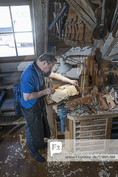 Craftsman carving violin from wood at workshop