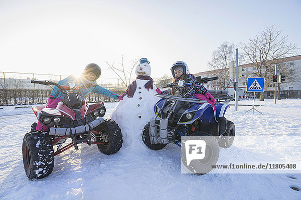 Girls riding quad bike and leaning on snowman