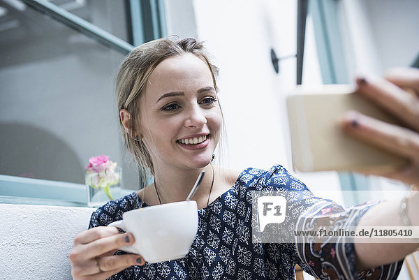 Young woman holding coffee cup and taking self portrait at restaurant
