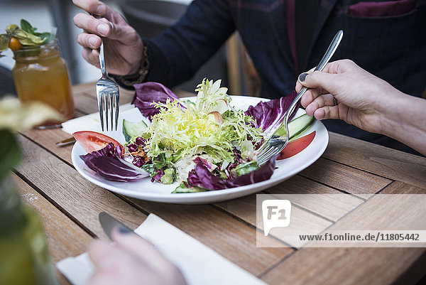 Cropped image of two people holding fork and eating salad