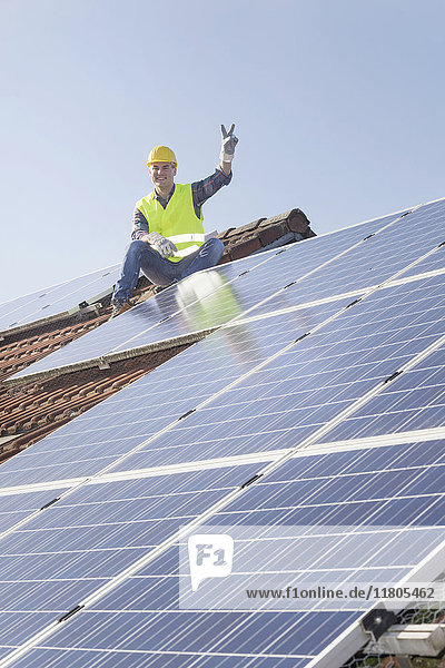 Ingenieur macht eine Friedensgeste  während er eine Pause von der Installation von Solarzellen auf dem Hausdach macht