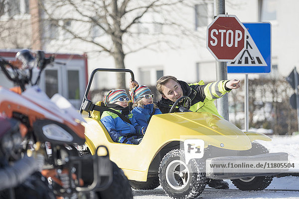 Man teaching boys to drive electric toy car