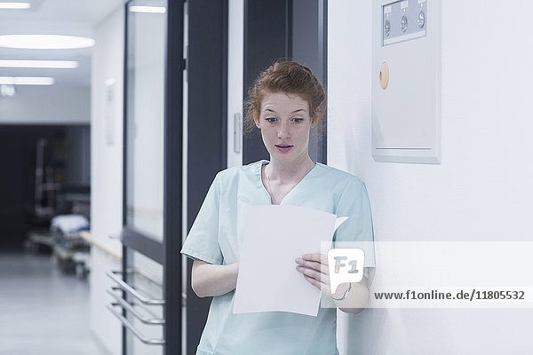 Shocked nurse reading medical chart while leaning by wall