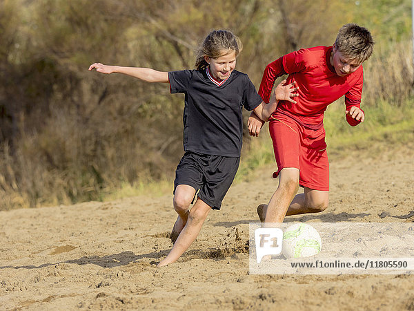Girl and boy chasing soccer ball across sand