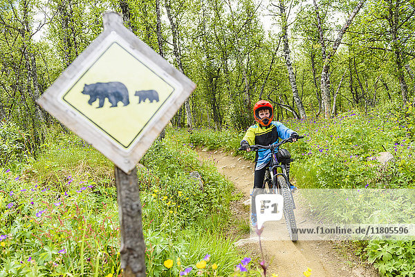 Junge auf dem Fahrrad  im Vordergrund ein Schild mit einem kreuzenden Bären