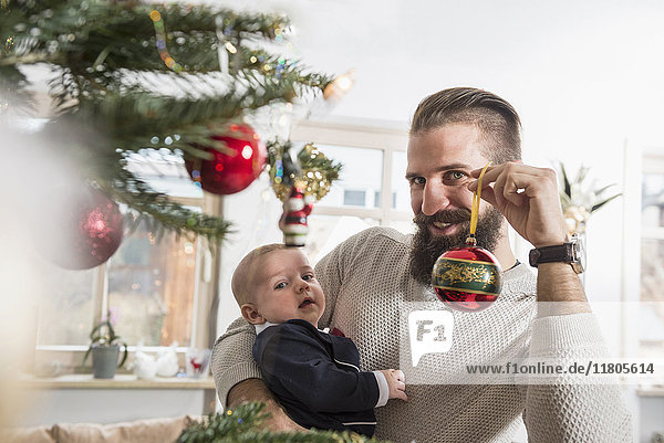Porträt eines Vaters  der einen kleinen Jungen und eine Weihnachtskugel hält