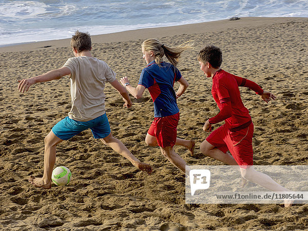 Girl and boys playing soccer on shore at the beach