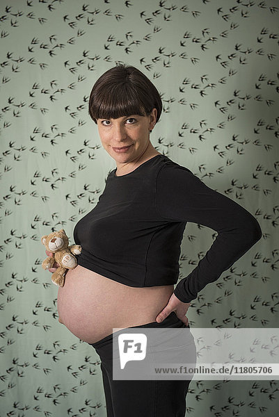 Porträt einer schwangeren Frau  die ein Plüschtier auf dem Bauch hält und die Hand auf die Hüfte legt