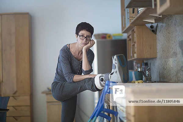Portrait of woman resting her broken leg on kitchen worktop