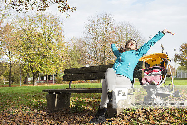 Mother stretching while sitting on bench in park by stroller