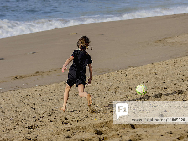 Girl playing soccer on shore at beach